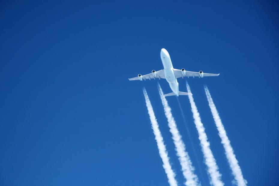 An airplane at altitude with fuel emissions streaming behind it