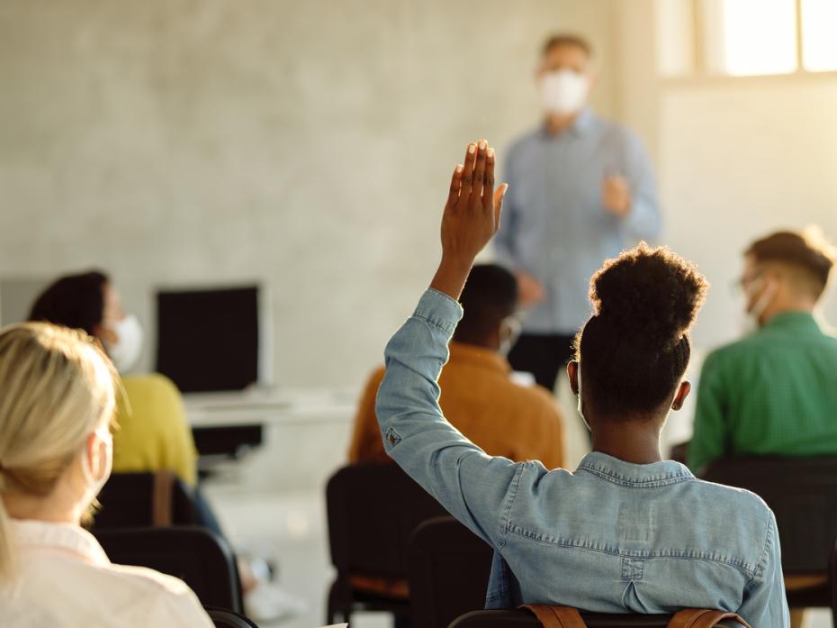 A black student raising their hand in class. 