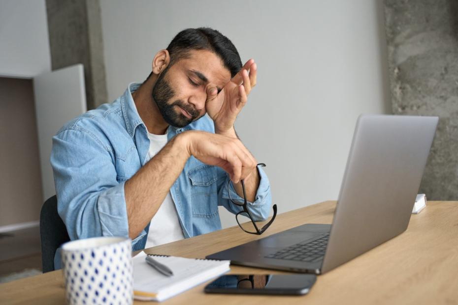 A tired looking man at his laptop rubbing his eyes 