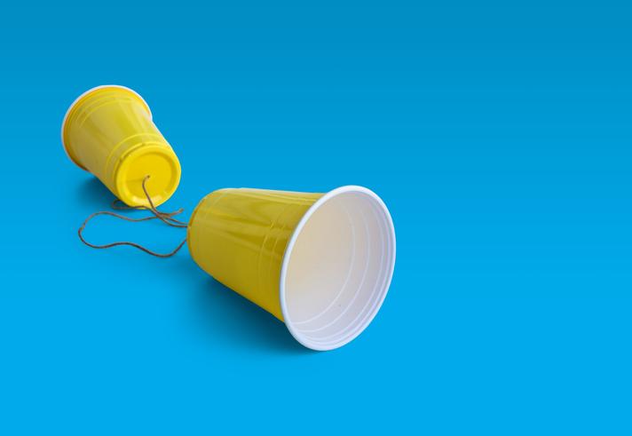 Two yellow cups joined by a string on a blue background