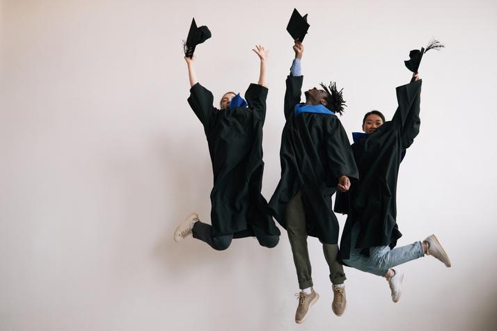 Three college students in graduation gowns jumping