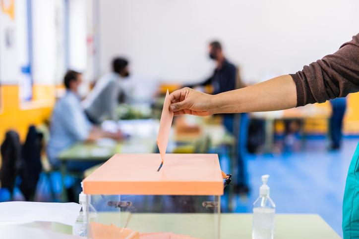 A hand places a vote inside a ballot box