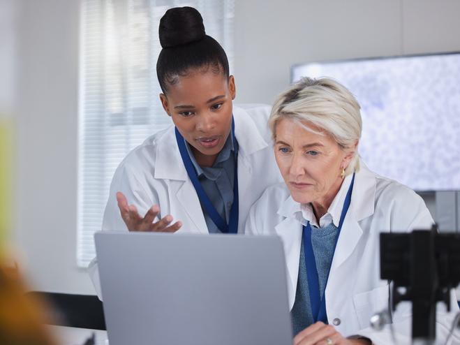 Two scientists in white coats discuss over a laptop