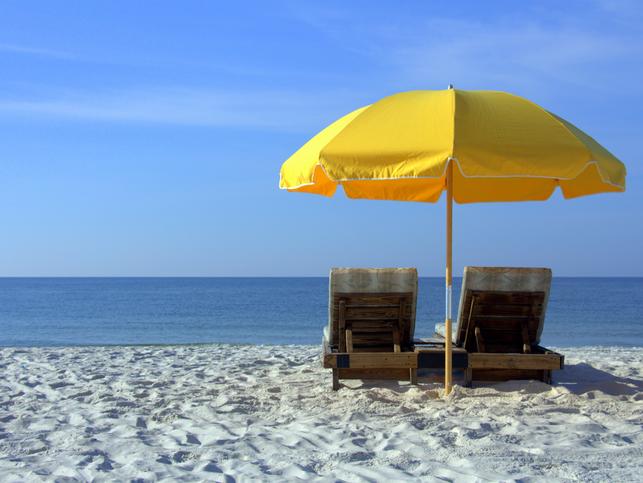 Two sun loungers sit on white sand, shaded by a yellow beach umbrella 