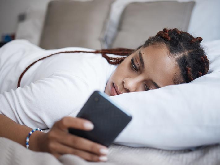 Young Black woman lying on bed looking at phone