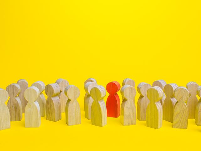 In a group of wooden toy people, a red one stands out