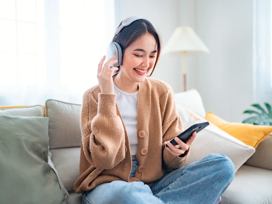 Young woman relaxing and using headphones to listen to a podcast in her living room