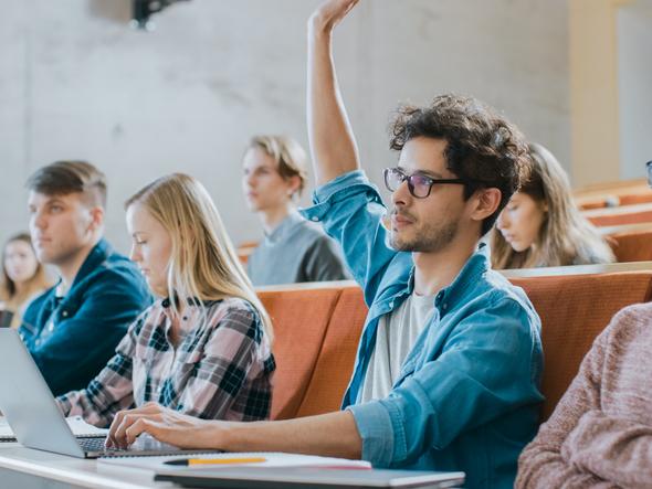 A student raises his hand in a lecture hall