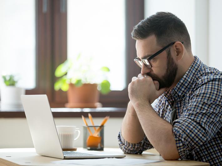 Millennial man thinking at laptop