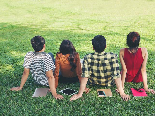 Four students sit on a grassy lawn