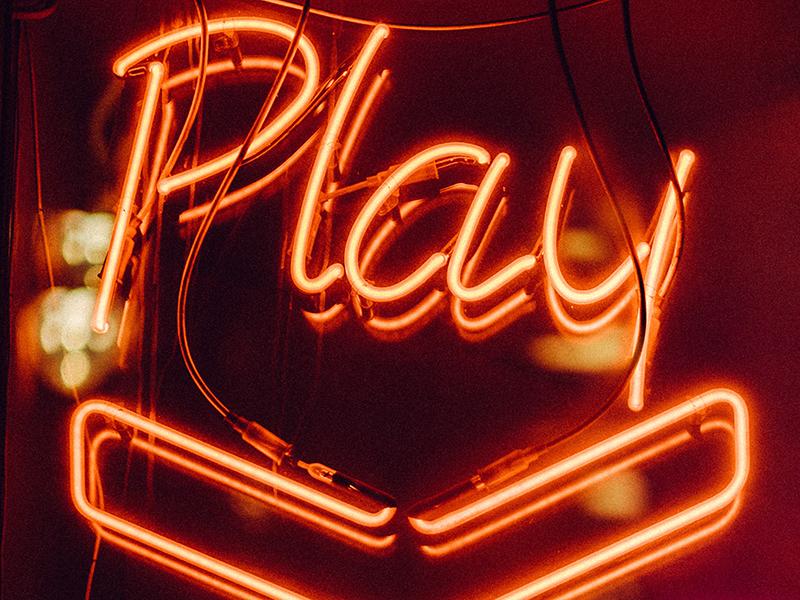 The word ‘play’ and a downward arrow in neon