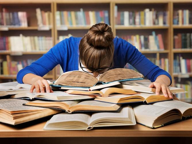 A PhD student falling asleep on their books in a higher education university - check out these five top tips for completing your thesis