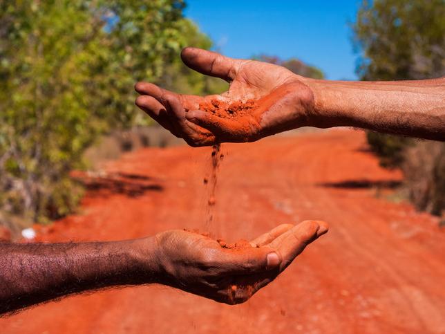 Australian aboriginal hands against red dirt road illustrating exchange of Indigenous wisdom