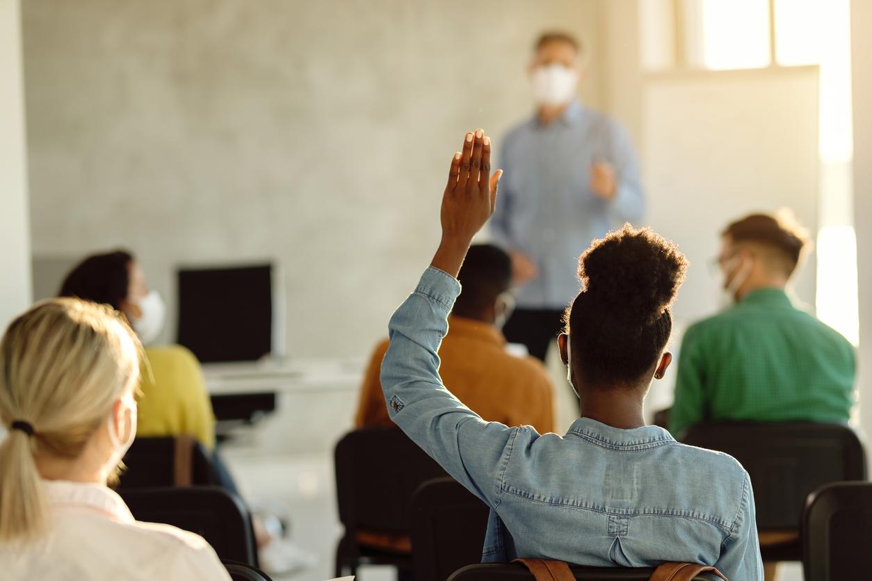 A black student raising their hand in class. 