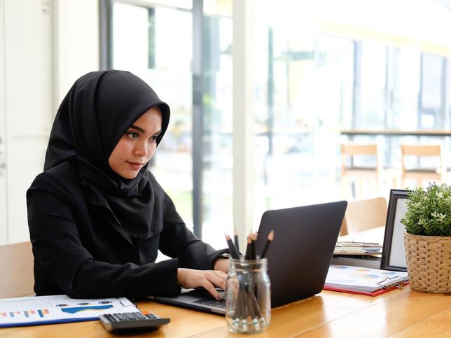 Young woman in black hijab working at laptop
