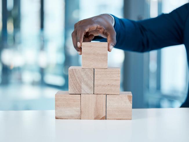 Black man in suit puts wooden block on top of pile