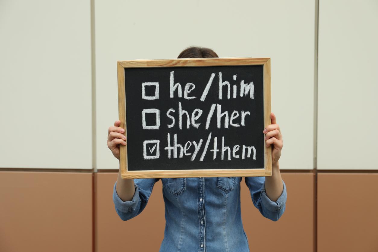 Image of a non-binary person holding up a sign showing their pronouns