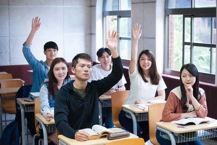 Asian students raising hands in university class