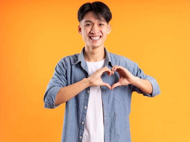 Male Asian student making heart symbol with his hands