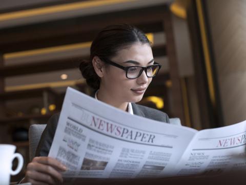 Female student wearing glasses reading a newspaper