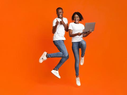 Two young people jumping, one is holding a laptop