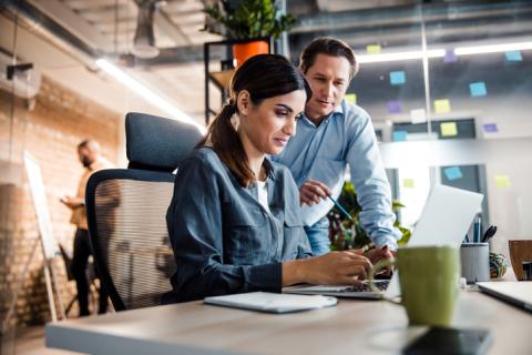 A man helps a woman working at a laptop