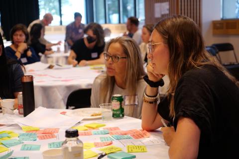 Two people sit at a table covered with post-it notes at an event