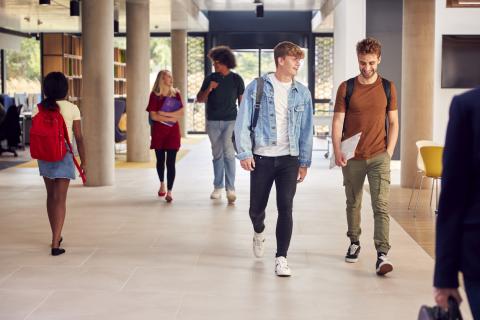 Two male students talking while walking together along a corridor in their university building