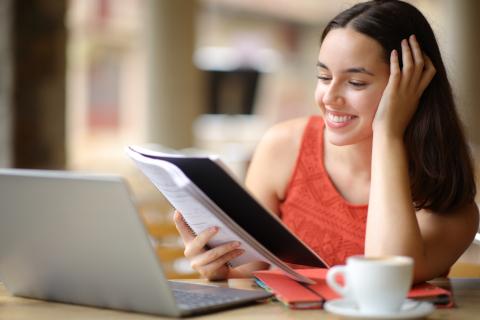 A young woman referring to her notes while stufying at home on her laptop