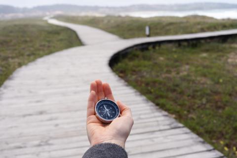 A hand holds out a compass in front of a divided path