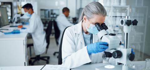 A woman in a research lab looking through a microscope