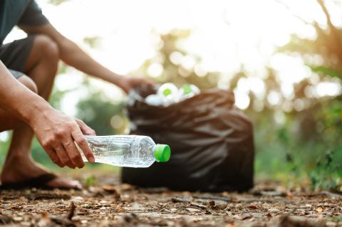 A hand picking up a plastic bottle off the ground