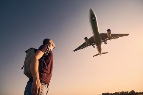 Young male with backpack looking up at a plane overhead