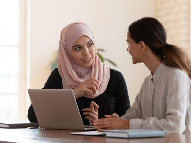 two young women talking over a laptop