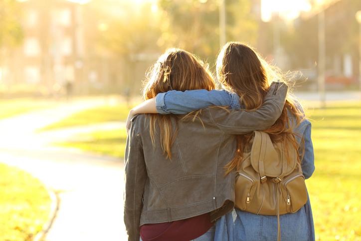 Two women walk away from the camera, their arms around each other's shoulders