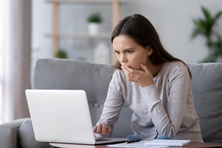 A woman looks shocked as she browses a laptop