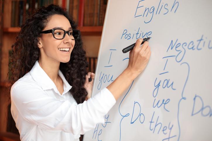 A teacher writes English phrases on a whiteboard