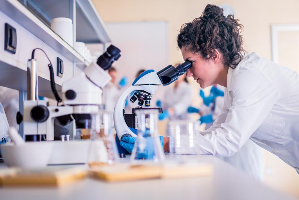 An early career researcher looking through a microscope in a lab