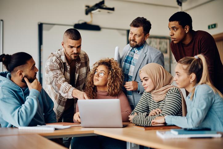 A group of students gather round a laptop