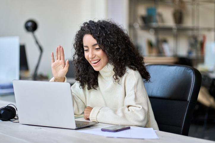 A woman waves to others over a video call