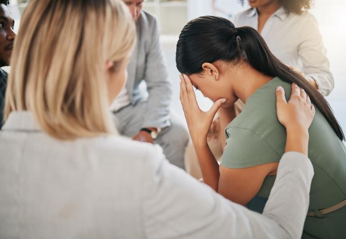 A group comforts a woman, sitting with her head bowed