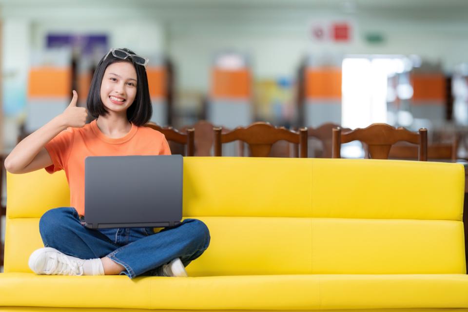 Student sitting on a sofa with her laptop with a thumbs up