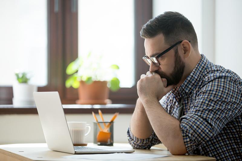 Millennial man thinking at laptop