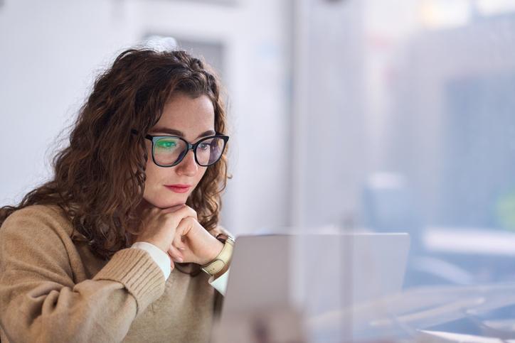 A young woman in glasses works at a laptop