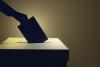A shadowy hand casts a vote in a ballot box