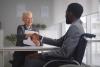 Black male job candidate in a wheelchair shaking hands with mature white woman