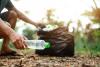 A hand picking up a plastic bottle off the ground